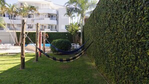 Una hamaca en un área con césped, un seto y un edificio al fondo.