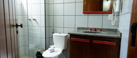 A bathroom with a toilet, a sink, a mirror, and a shower area.