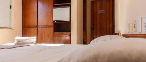 A hotel room with a bed, a wooden wardrobe, and a door with a number sign.