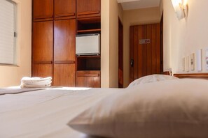 A hotel room with a bed, a wooden wardrobe, and a door with a number sign. - HANNA Praia Hotel (Florianópolis)