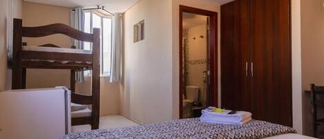 Un dormitorio con una cama nido, una cama individual con colcha estampada, un armario de madera y un baño visible a través de una puerta abierta.