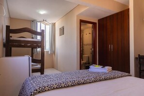 A bedroom with a bunk bed, a single bed with a patterned bedspread, a wooden wardrobe, and a bathroom visible through an open door. - HANNA Praia Hotel (Florianópolis)