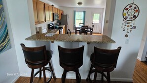 A kitchen with wooden cabinets, a granite countertop, and a dining area with a table and chairs. - Acadia Villas!  2A Hunter's Way with EV Charger. (Trenton)