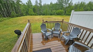 A wooden deck with four Adirondack chairs and a small table, surrounded by a grassy yard and a white fence. - Acadia Villas!  2A Hunter's Way with EV Charger. (Trenton)