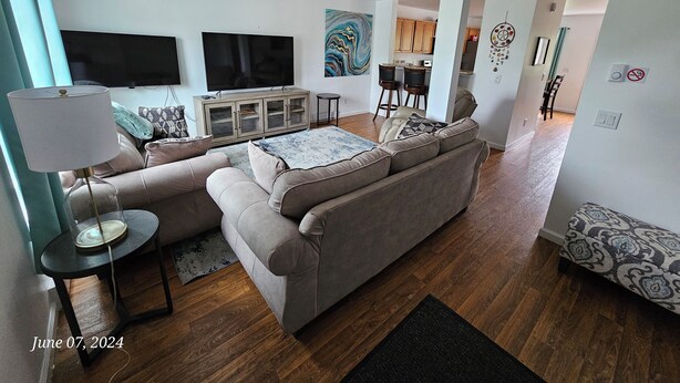 A modern living room with a sectional sofa, a flat-screen TV, a ceiling fan, and a dining area with a kitchen in the background. - Acadia Villas!  2A Hunter's Way with EV Charger. (Trenton)
