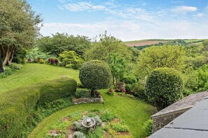 A well-maintained garden with neatly trimmed hedges, a stone fountain, and a variety of shrubs and trees. - 4 Bed in Goodleigh (oc-e29107) (Goodleigh)