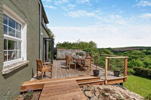 Eine Holzterrasse mit Gartenmöbeln, eine Steinmauer und Blick ins Grüne.