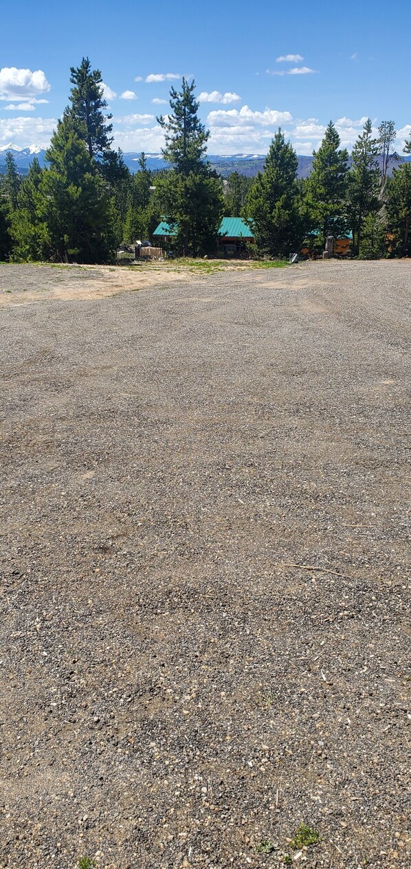 Un espace de stationnement recouvert de gravier, d’où l’on peut admirer une chaîne de montagnes et quelques bâtiments au loin.
