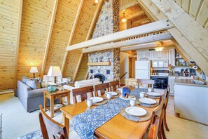 A cozy interior with a dining area, kitchen, and living space, featuring wooden beams and stone accents. - Upper Peninsula Lakefront A-Frame Cabin w/ Dock (Channing)
