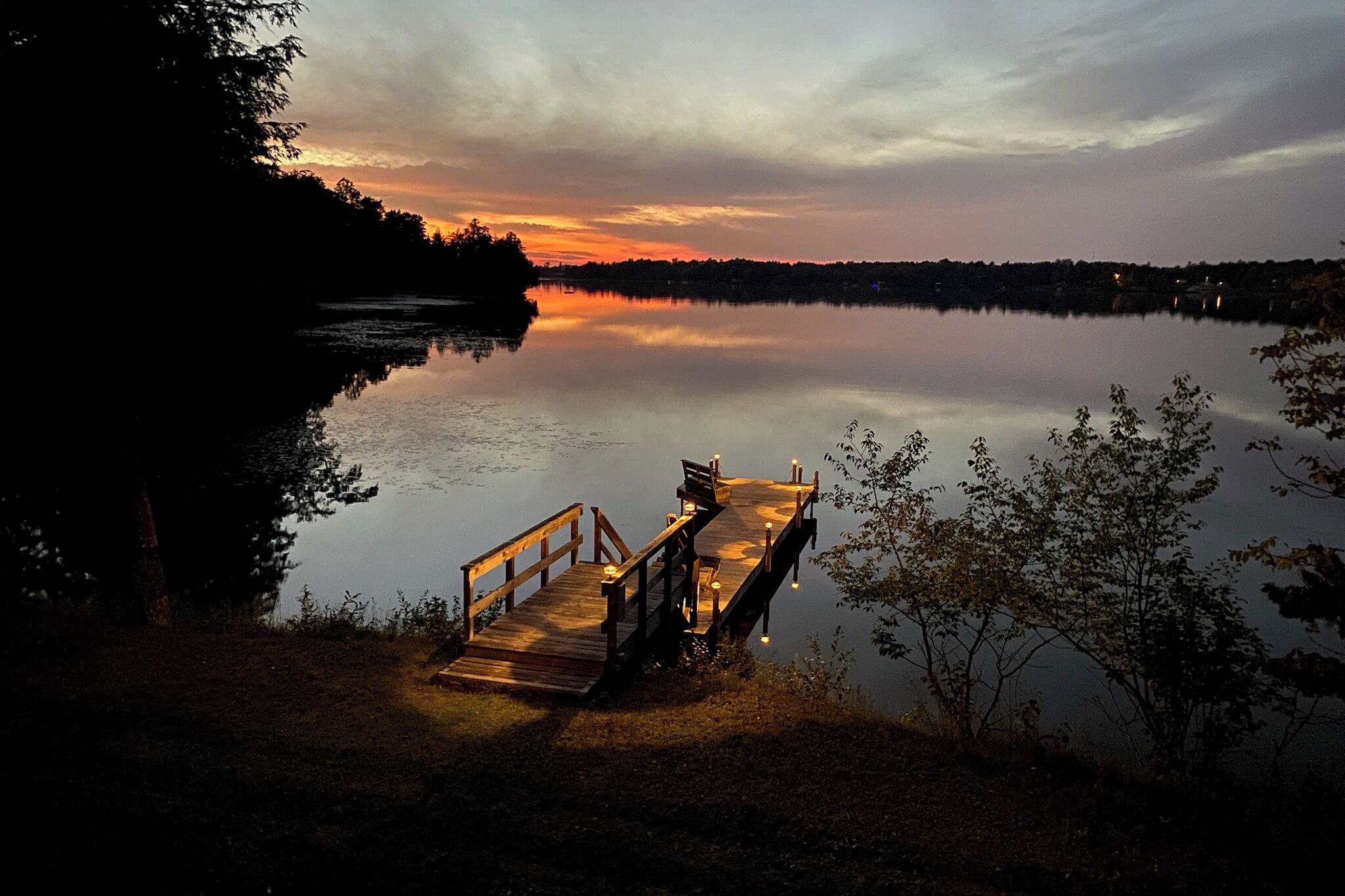 Une jetée en bois s’étendant sur un lac paisible au crépuscule, avec un coucher de soleil en arrière-plan.