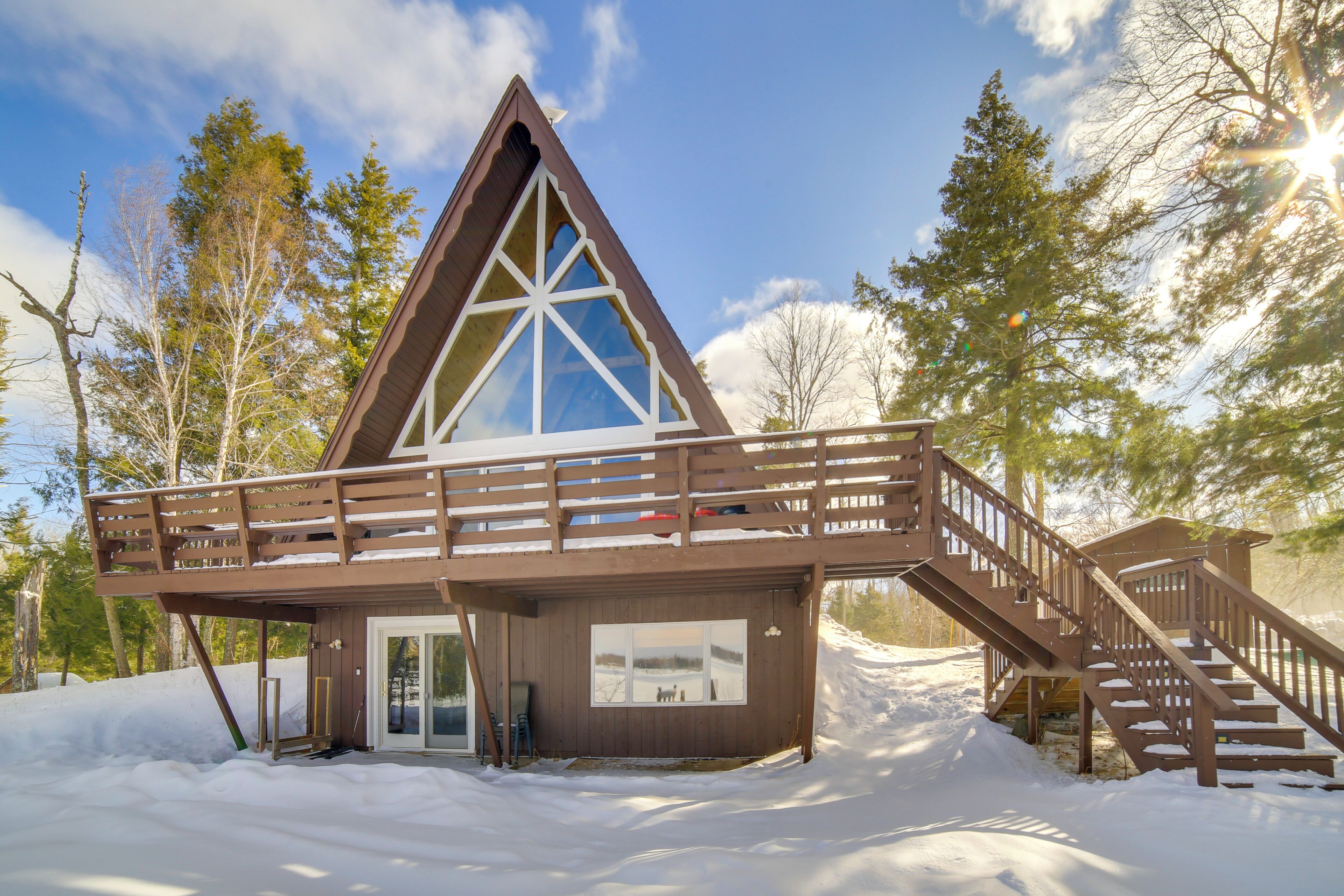 Une cabane en bois avec un toit triangulaire, un balcon et un escalier menant à une terrasse.