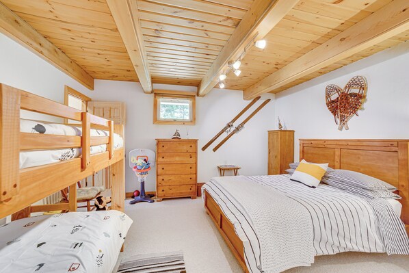 Une chambre confortable avec un lit superposé, un lit simple, une tête de lit en bois, une petite fenêtre et un porte-skis.