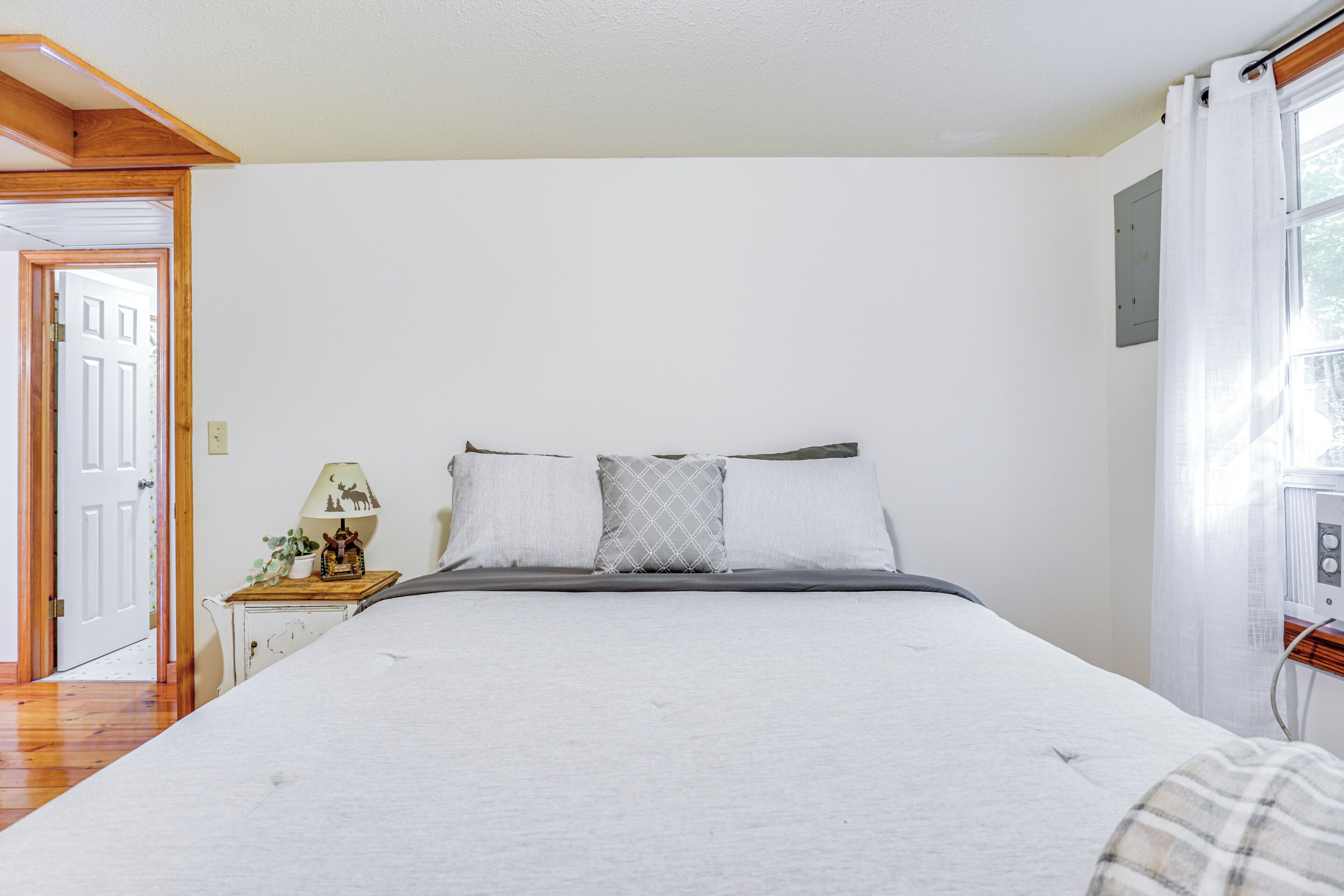 Een slaapkamer met een groot bed, een nachtkastje met een lamp en een raam met gordijnen.