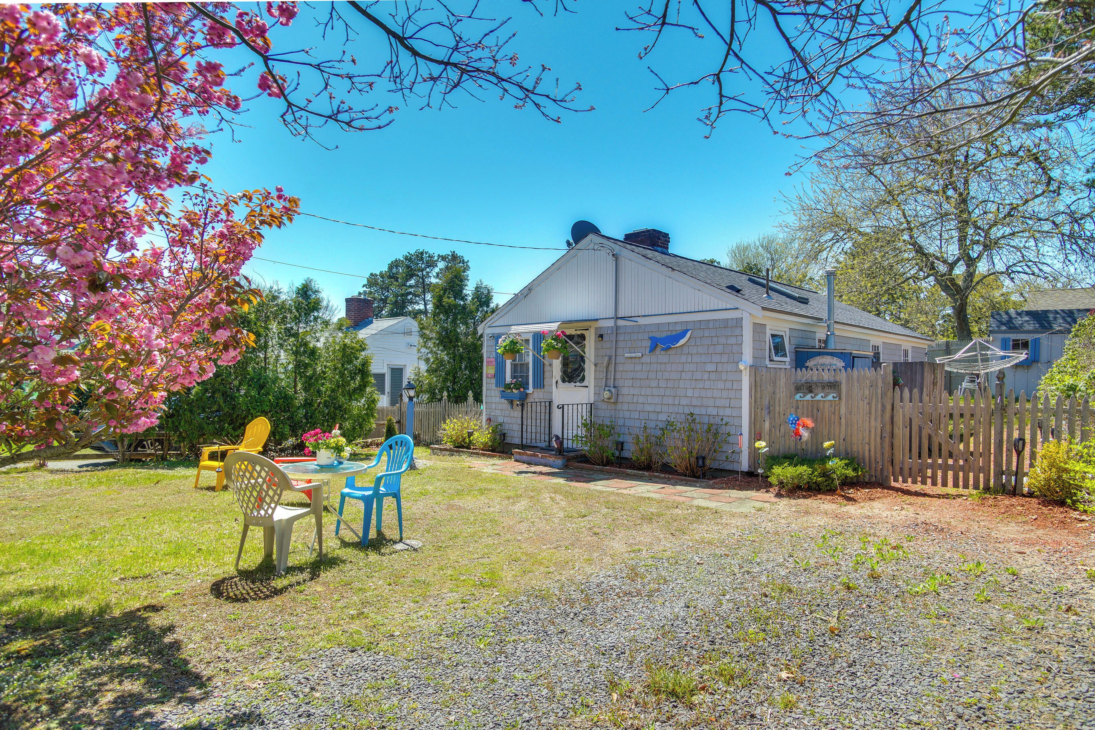 A house with a gravel driveway, a wooden fence, and a garden with chairs and flowers.