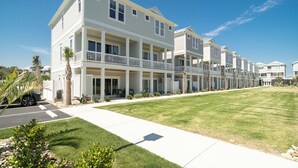 A row of two-story townhouses with balconies, a grassy lawn, and a clear blue sky. - Just steps away - beach, pool, & attractions on the Emerald Isle! New Home.  (Emerald Isle)