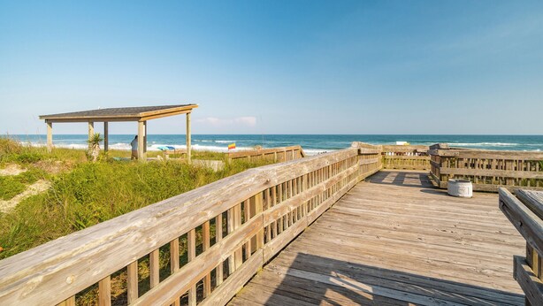 A wooden boardwalk leading to a beach with a wooden structure. - Just steps away - beach, pool, & attractions on the Emerald Isle! New Home.  (Emerald Isle)