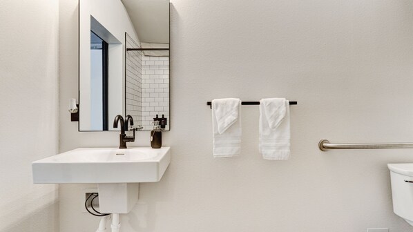Ein Badezimmer mit einem weißen Waschbecken, einem Spiegel und zwei weißen Handtüchern, die an einer Handtuchstange hängen.