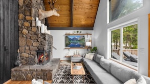 A cozy living room with a stone fireplace, a large window, and a view of the outdoors.