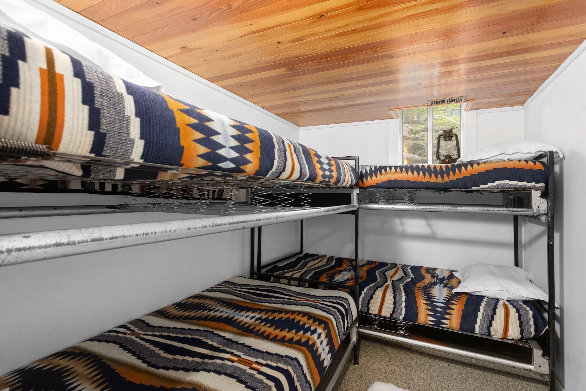 A bunk bed room with patterned blankets and a wooden ceiling.