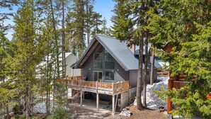 A cabin with a wooden deck, surrounded by tall trees and a rocky landscape.