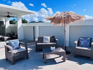 Een terras buiten met rieten meubilair, een plafondventilator en een rieten zonnescherm.