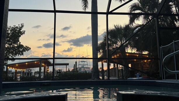 A pool area with a view of palm trees and a sunset. - Waterfront Home on the Harbor with a Pool, Boat Dock & Pet Friendly! (Stuart)