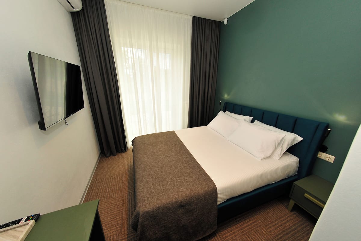 Ein Hotelzimmer mit Bett, Fernseher, Nachttisch und einem Fenster mit Vorhängen.