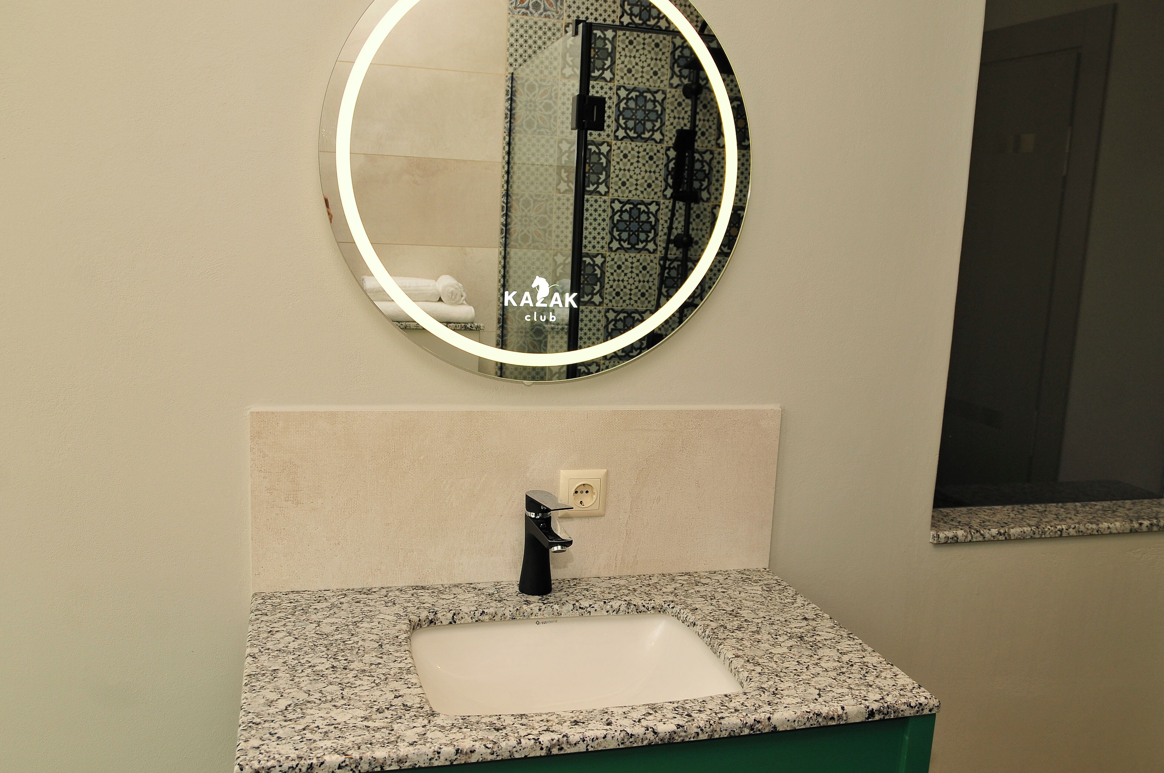 A bathroom with a round mirror, a sink with a black faucet, and a towel rack.