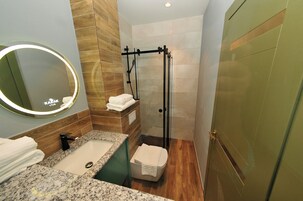 Un baño con encimera de granito, lavabo, espejo con luz, toallero, cabina de ducha de vidrio y suelo de madera.