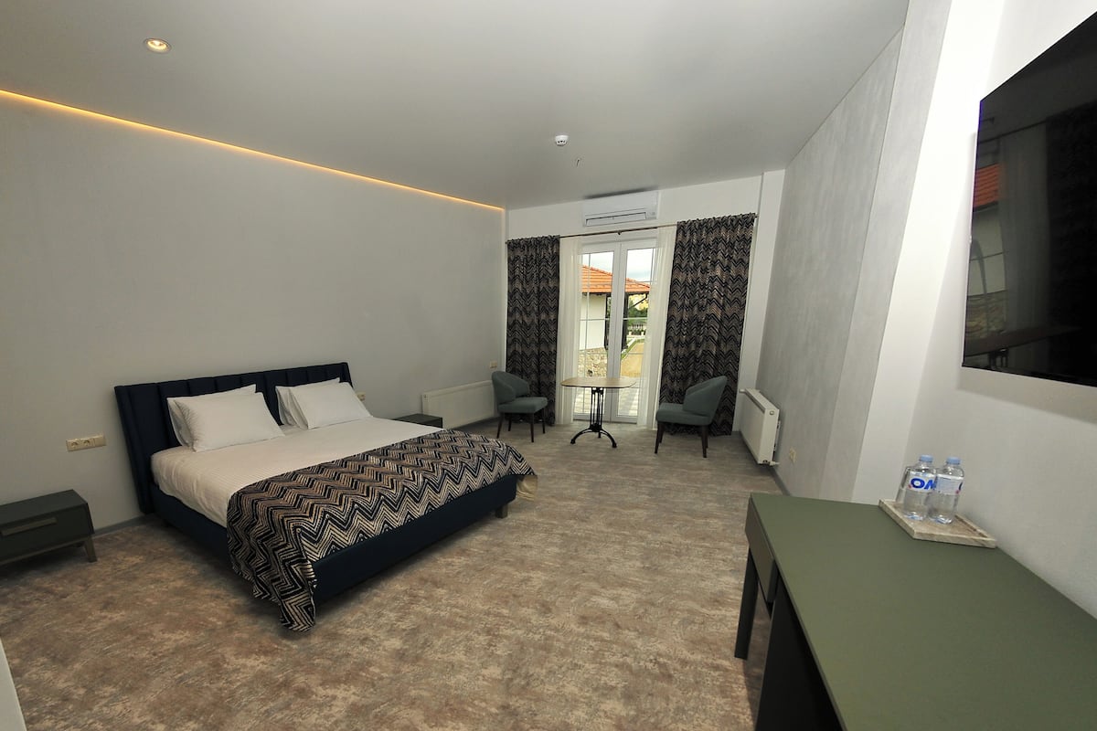 Ein modernes Hotelzimmer mit einem Bett, einem kleinen Tisch, zwei Stühlen und Blick ins Freie.