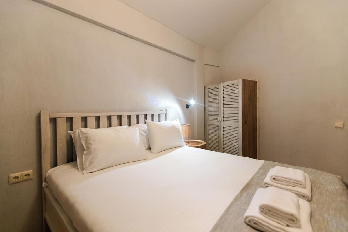 Ein ordentlich bezogenes Bett mit weißen Leinen und Kissen, eine Nachttischlampe und ein Holz-Kopfteil.