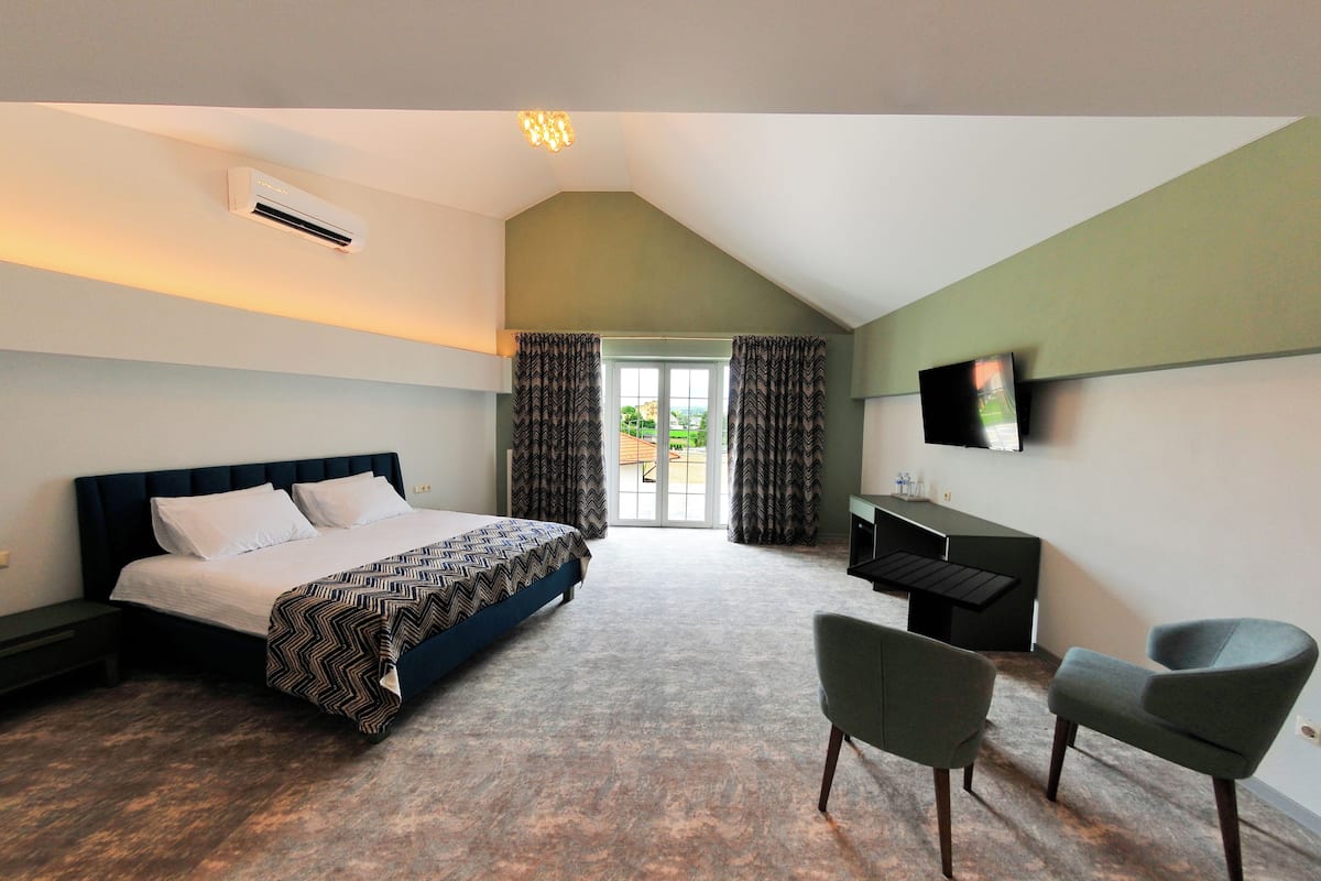 Ein Schlafzimmer mit einem Bett, einem Schreibtisch, zwei Stühlen, einem Fernseher und einem Fenster mit Vorhängen.