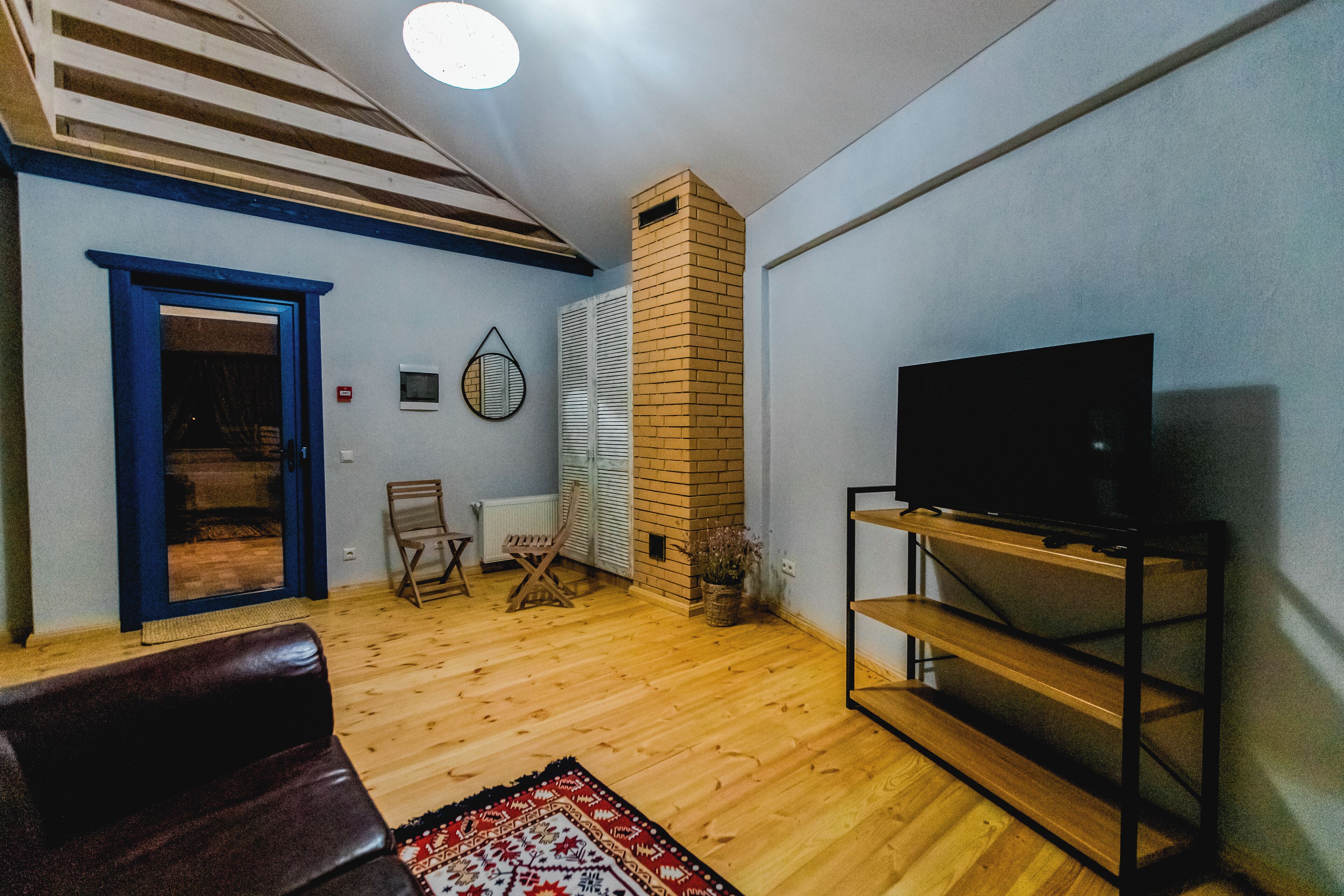 A living room with a wooden floor, a TV on a stand, a blue door, and a brick fireplace.
