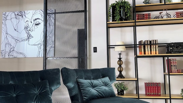 Una sala de estar moderna con un sofá modular, un panel decorativo y una estantería con varios objetos.