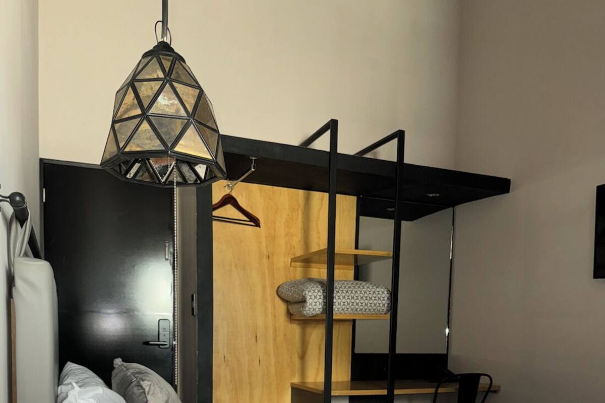 Een kleine kamer met een bed, een houten hoofdbord, een hanglamp en een klein houten plankje.