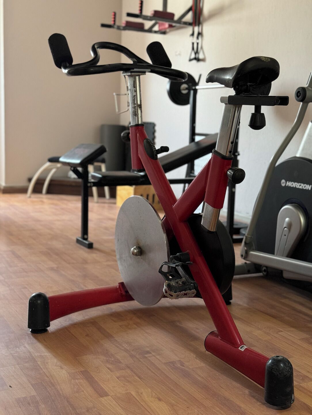 A stationary bike with a red frame and black handlebars in a gym with wooden flooring and exercise equipment in the background.