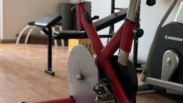 A stationary bike with a red frame and black handlebars in a gym with wooden flooring and exercise equipment in the background.