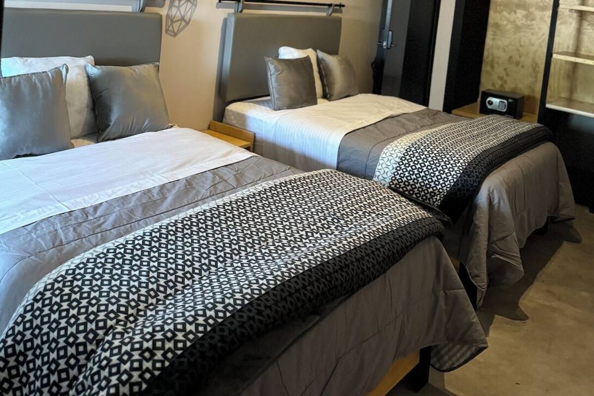 Een hotelkamer met twee bedden, een nachtkastje, een lamp en een raam met gordijnen.