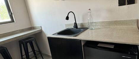 Eine kleine Küche mit einem schwarzen Geschirrspüler, einem Spülbecken und einem Holzregal darüber.