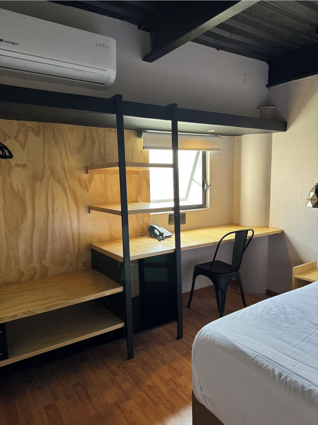 Una cama litera con escritorio y silla, una ventana pequeña y una cama.