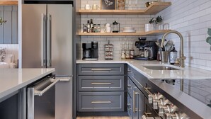 Une cuisine moderne avec des meubles de couleur grise, un réfrigérateur en acier inoxydable, une machine à café et un évier doté d’un robinet doré.