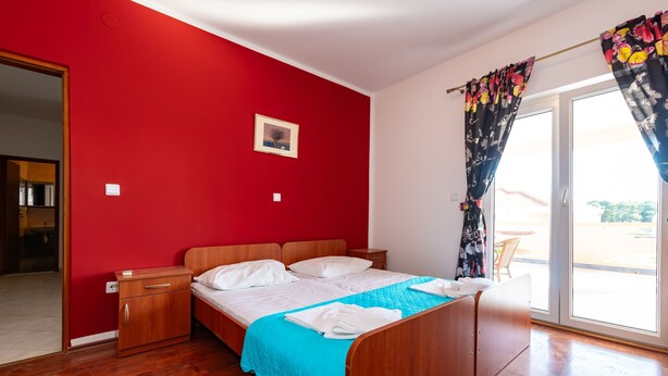 A room with a wooden bed, a red wall, and a view through a glass door. - Bonvie Apartments in Center B4 (Novalja)