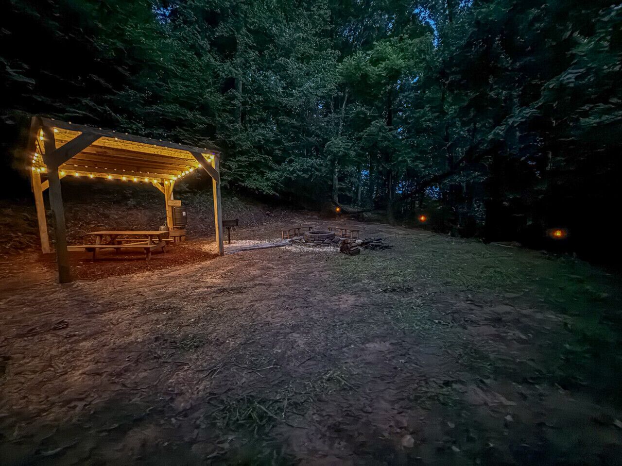 Un gazebo in legno con luci a catena, immerso in una zona boschiva.
