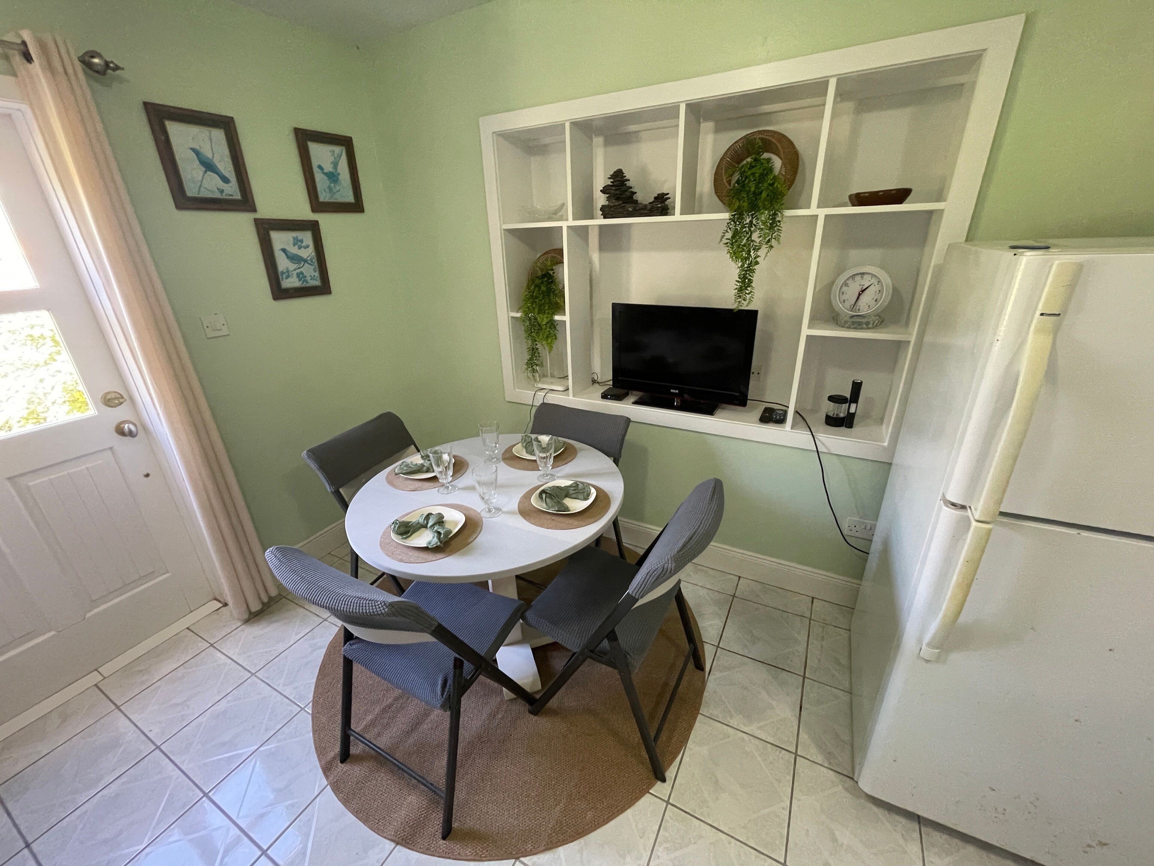A dining area with a round table, four chairs, and a white refrigerator.