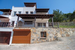A multi-story building with a stone facade, a wooden garage door, and a balcony with a metal railing. - Villa Bambaska (Milas)