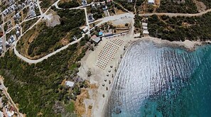An aerial view of a coastal area with a beach, a parking lot, and a small building with a red roof. - Villa Bambaska (Milas)