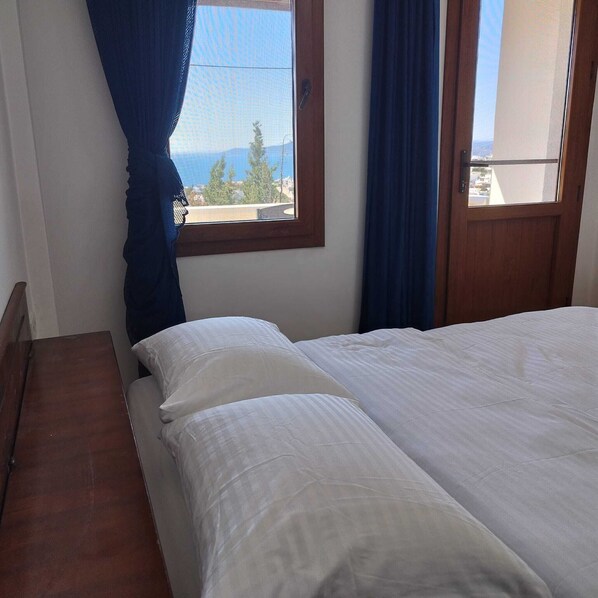 Un dormitorio con cama, ventana con cortinas y vista al mar.