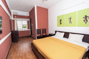 A room with a bed, a desk, and a chair. There is a window with curtains, a radiator, and a wall-mounted air conditioner. - Deep Woods Stay (Kinathukadavu)