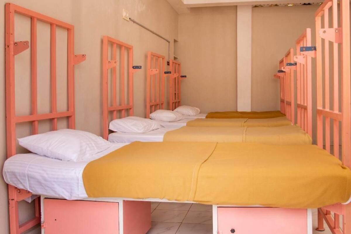 A row of pink bunk beds with white bedding and yellow blankets, in a room with plain walls and a tiled floor.