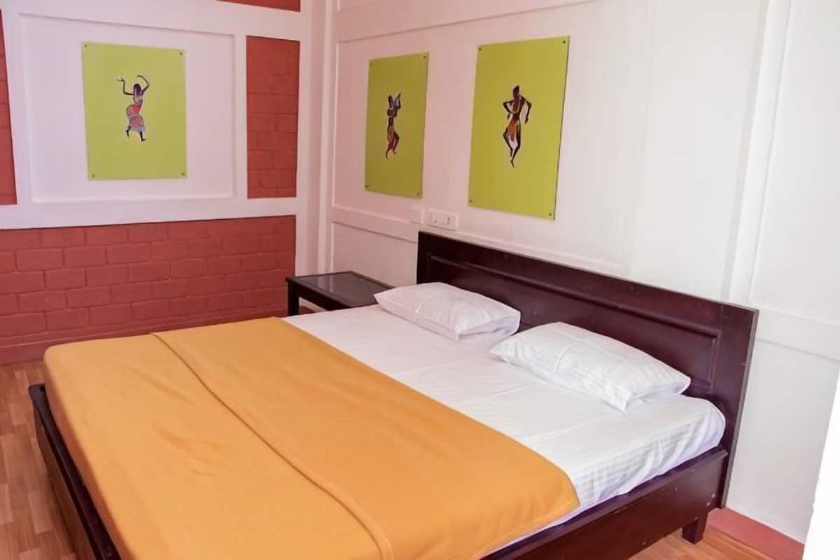 Una cama con cabecera de madera, almohada blanca, manta amarilla y obras de arte en las paredes.